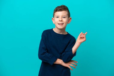 Küçük çocuk mavi arka planda izole edilmiş, mutlu ve dik duruyor.