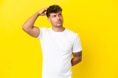 Kafkasyalı yakışıklı genç adam sarı arka planda izole edilmiş, kafası kaşınırken şüpheleri var.