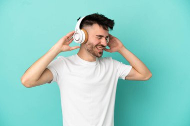 Kafkasyalı genç adam mavi arka planda izole edilmiş müzik dinliyor ve şarkı söylüyor.