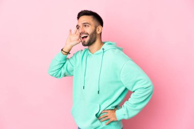 Pembe arka planda izole edilmiş genç beyaz adam elini kulağına koyarak bir şeyler dinliyor.
