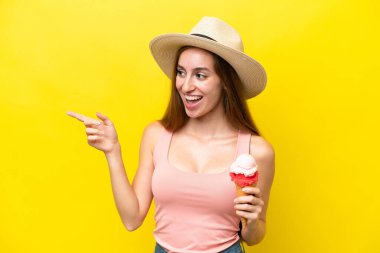 Sarı arka planda izole edilmiş kornet dondurması olan beyaz bir genç parmak göstererek bir ürün sunuyor.