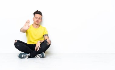 Beyaz bir adam yerde oturuyor ve jestleri durduruyor.