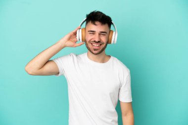 Genç beyaz adam mavi arka planda izole edilmiş müzik dinliyor.