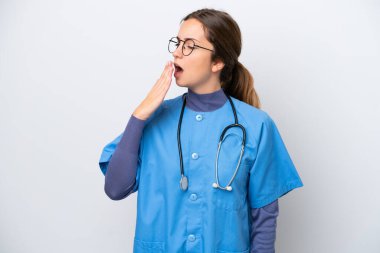 Beyaz arka planda izole edilmiş beyaz bir hemşire kadın esniyor ve ağzı açık bir şekilde elleriyle ağzını kapatıyor.