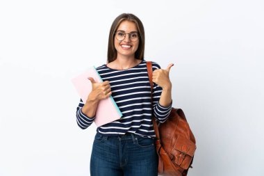 Beyaz arka planda izole edilmiş genç bir bayan. Baş parmakları havada ve gülümsüyor.