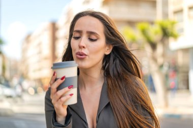 Açık havada elinde kahve tutan genç bir kadın.