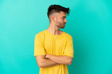 Mavi arka planda izole genç beyaz adam kollarını çapraz tutuyor.