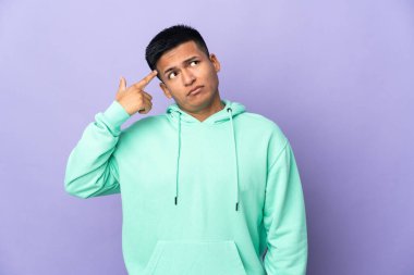 Genç Ekvador 'lu, mor arka planda izole edilmiş. Delilik jesti yapıyor. Parmağını kafaya koyuyor.