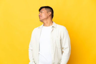 Genç Ekvadorlu adam sarı arka planda izole edilmiş, yana bakıyor ve gülümsüyor.