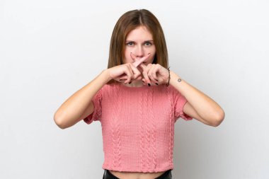 Beyaz arka planda izole edilmiş genç bir İngiliz kadın sessizlik işareti gösteriyor.