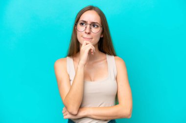 Kafkasyalı genç bir kadın mavi arka planda izole edilmiş. Şüpheleri ve düşünceleri var.
