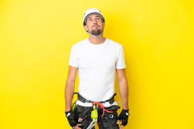 Genç kaya tırmanışçısı sarı arka planda izole edilmiş ve yukarı bakıyor.