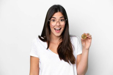 Elinde Bitcoin tutan genç Brezilyalı kadın beyaz arka planda şaşırmış ve şok olmuş bir yüz ifadesi ile izole edilmiş.