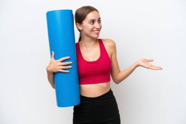 Beyaz bir zemin üzerinde yalıtılmış bir minder tutarken yoga derslerine giden beyaz, beyaz, beyaz bir kadın.