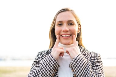 Açık havada gülümseyen mutlu ve hoş bir ifadeyle genç sarışın kadın.