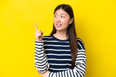 Sarı arka planda izole edilmiş genç Çinli kadın harika bir fikre işaret ediyor.