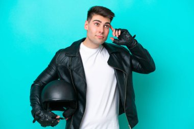 Motosiklet kasklı genç beyaz adam mavi arka planda izole edilmiş. Şüpheleri ve düşünceleri var.