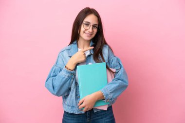 Pembe arka planda izole edilmiş genç Ukraynalı kadın bir ürünü sunmak için kenarı işaret ediyor.