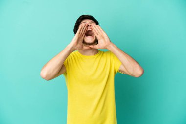 Genç Rus adam mavi arka planda izole edilmiş bağırıyor ve bir şey duyuruyor.