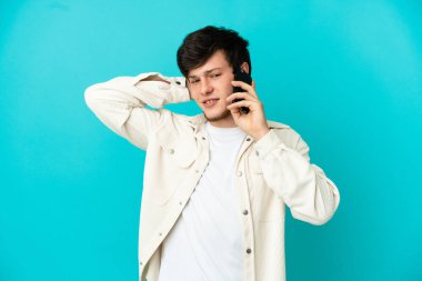 Mavi arka planda izole edilmiş cep telefonu kullanan genç Rus adamın şüpheleri var.