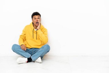 Beyaz arka planda izole bir şekilde yerde oturan genç Afrikalı Amerikalı adam ağzı açık bağırıyordu.