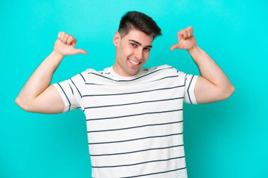 Kafkasyalı genç adam mavi arka planda soyutlanmış gururlu ve kendini beğenmiş.