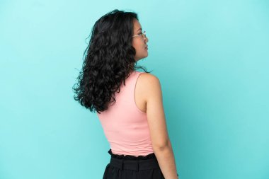 Genç Asyalı kadın mavi arka planda izole edilmiş. Arka tarafta ve yan tarafa bakıyor.