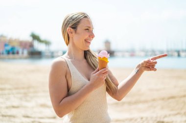 Açık havada kornet dondurmalı genç sarışın bir kadın bir ürün sunmak için yan tarafı işaret ediyor.