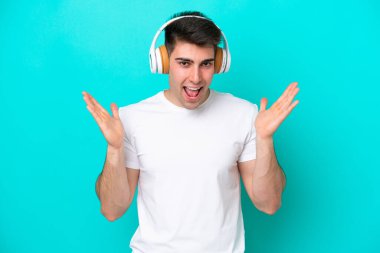 Mavi arka planda izole edilmiş genç beyaz adam şaşırdı ve müzik dinliyor.