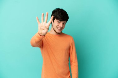 Genç Rus adam mavi arka planda izole edilmiş mutlu ve parmakları olan dört kişi sayıyor.