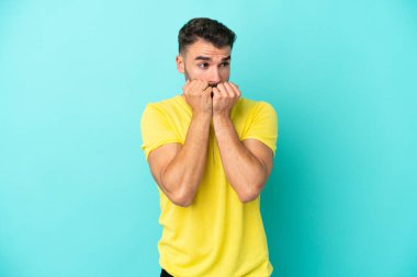 Mavi arka planda izole edilmiş genç beyaz bir adam gergin ve korkmuş bir şekilde elleriyle suni teneffüs yapıyor.