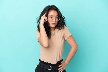 Asyalı genç bir kadın mavi arka planda izole edilmiş bir fikir düşünüyor.