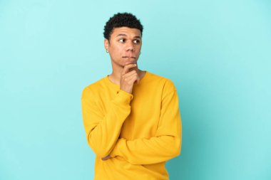 Genç Afrikalı Amerikalı adam mavi arka planda izole edilmiş. Şüpheleri ve düşünceleri var.