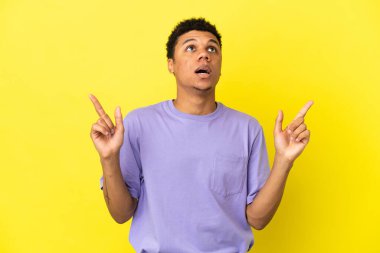 Sarı arka planda izole edilmiş genç Afrikalı Amerikalı şaşırmış ve işaret ediyor.