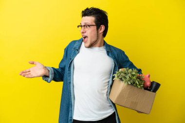 Rus adam, sarı arka planda izole edilmiş şeylerle dolu bir kutuyu kaldırırken sürpriz bir ifadeyle yan tarafa bakıyordu.