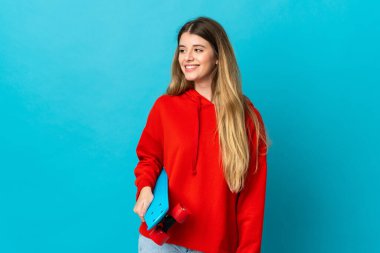 Genç sarışın kadın mavi arka planda tek başına paten kayıyor.