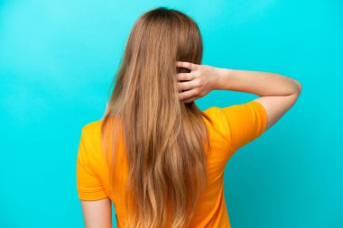 Kafkasyalı genç bir kadın mavi arka planda izole edilmiş ve düşünüyor.