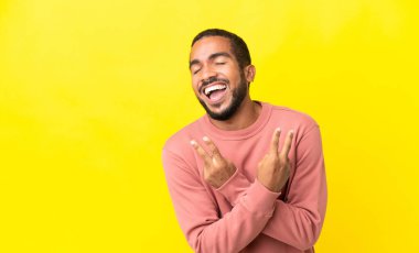 Sarı arka planda izole edilmiş genç latin adam gülümsüyor ve zafer işareti gösteriyor.