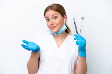 Beyaz arka planda izole edilmiş araçları tutan beyaz dişçi kadın ellerini kaldırırken şüphe duyuyor