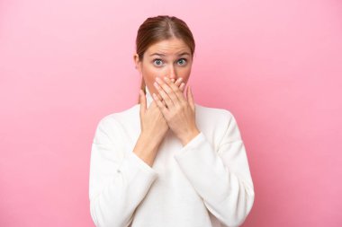 Pembe arka planda izole edilmiş genç beyaz kadın elleriyle ağzını kapatıyor.
