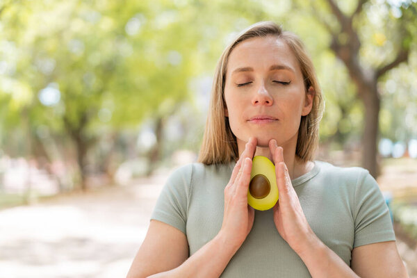Молодая блондинка на улице держит авокадо