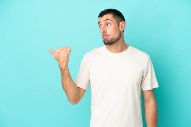 Mavi arka planda izole edilmiş yakışıklı beyaz adam mutsuzdu ve yüzünü gösteriyordu.