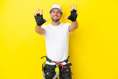 Genç kaya tırmanışçısı sarı arka planda izole edilmiş dokuzlu parmaklarla sayıyor.