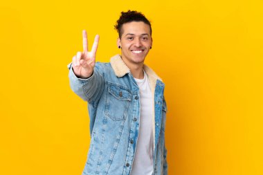 İzole edilmiş arka planda gülümseyen ve zafer işareti gösteren beyaz bir adam.