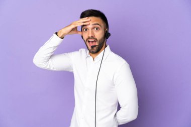 Mor arka planda izole edilmiş bir kulaklıkla çalışan pazarlamacı yan tarafa bakarken sürpriz jest yapıyor.