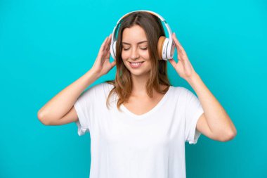 Genç beyaz kadın mavi arka planda izole edilmiş müzik dinliyor.