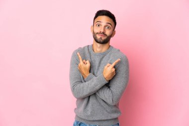 Pembe arka planda izole edilmiş genç beyaz adam, yan taraftakilerin şüphelerine işaret ediyor.