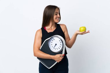 Genç Uruguaylı kadın beyaz arka planda izole edilmiş. Elma ararken bir tartı makinesi tutuyor.