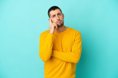 Mavi arka planda soyutlanmış yakışıklı, beyaz bir adam. Şüpheleri ve düşünceleri var.