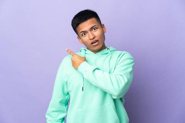 Genç Ekvadorlu, mor arka planda izole edilmiş, şaşırmış ve işaret eden bir adam.